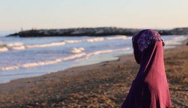 girl with the Arab veil to cover her head in the sea waiting for the arrival of the boat in summer
