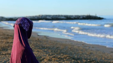 young girl with the Arab veil to cover her head by the sea awaits the arrival of the boat