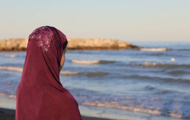 young girl with the Arab headscarf to cover her head by the sea awaits the arrival of friends on the boat