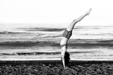 athletic young girl performs gymnastic exercises by the wheel on the beach by the sea with the Black & White effect