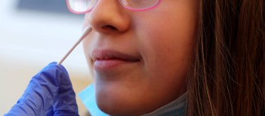 young caucasian girl in the clinic makes a swab in the nose to look for coronavirus clipart