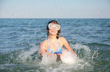 Tatlı beyaz kız deniz suyunda su sıçratıp sıçrıyor.