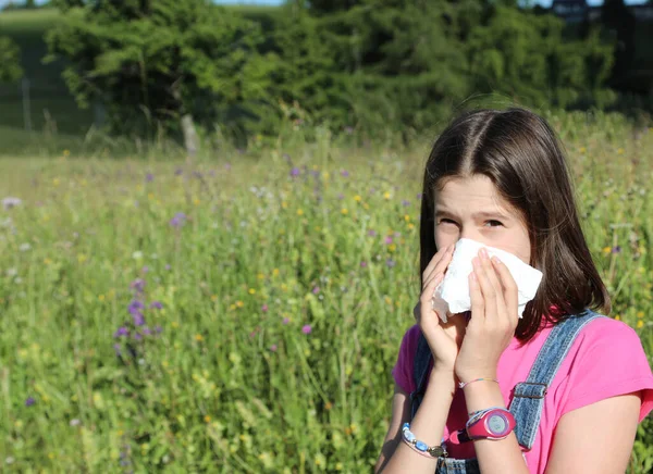 春に牧草地の真ん中で鼻を吹いて花粉にアレルギーを持つ少女 — ストック写真