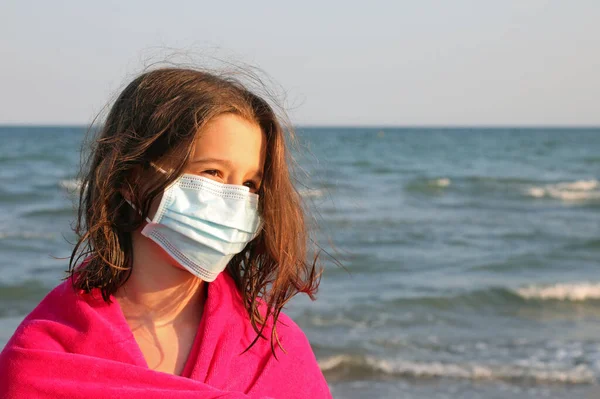 夏にリゾートのビーチでコロナウイルスから身を守るためにバスローブと外科マスクを持つ若い女の子 — ストック写真