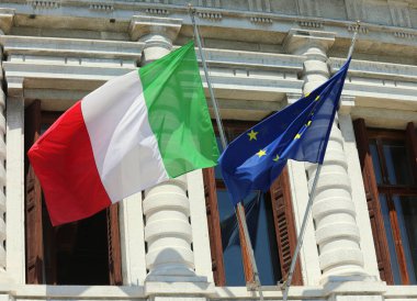 two large flags one Italian and one European flying outside the historic building during the international meeting