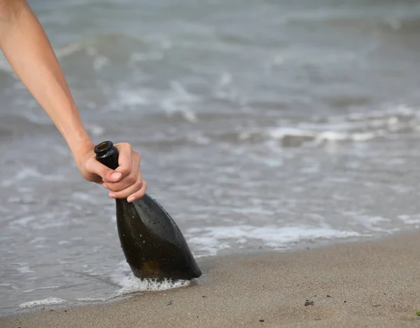 hand grabbing the beached glass bottle that can hold a secret message or the treasure map by the sea