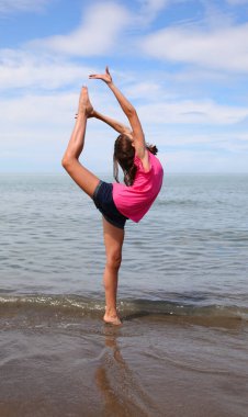 Genç beyaz kız yazın plajda ritmik jimnastik yapıyor.