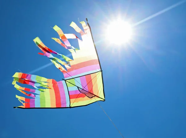 在蓝天高高地飘扬着五彩缤纷的大风筝 背光闪烁着灿烂的太阳 — 图库照片