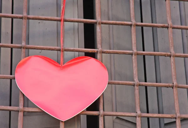 Red heart hanging on the grid of a window — Stock Photo, Image