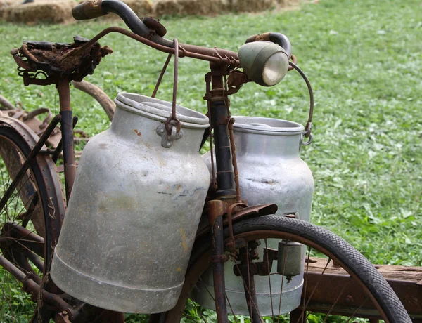 Rezavé kolo mlékař se dvěma starými mléko plechovky a rozbité sadd — Stock fotografie