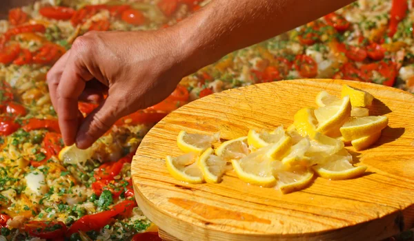 Cocinar pone rodajas de limón en la paella con mariscos y guisantes — Foto de Stock