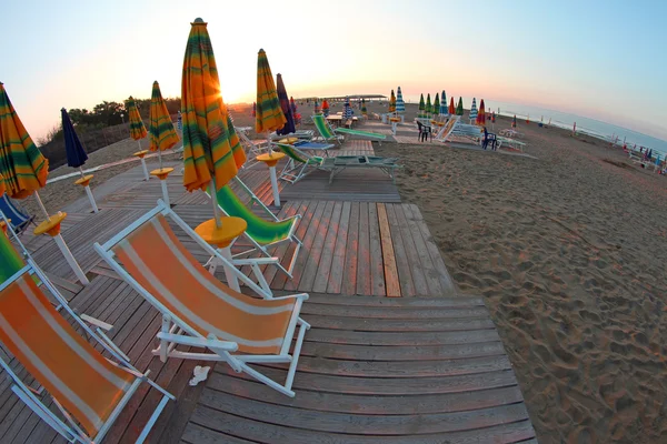 Sun rises on the beach still deserted, with Sun umbrellas a — Stock Photo, Image