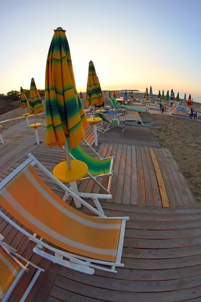 Słońce wschodzi na plaży wciąż opuszczony, z parasolami i słońce — Zdjęcie stockowe