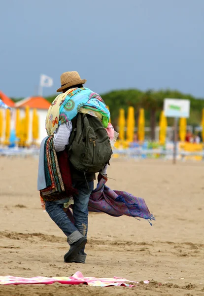 Abusive Peddler with fabrics and dresses walking on the beach — Stock Photo, Image