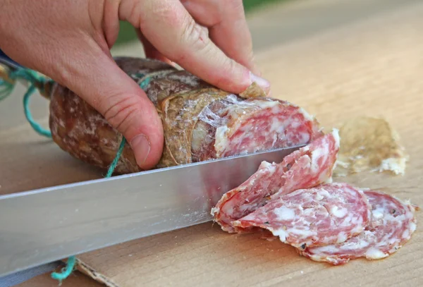 Cook's hand slicing the salami — Stock Photo, Image
