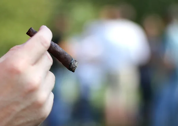 Main avec cigare et les gens en arrière-plan hors foyer — Photo