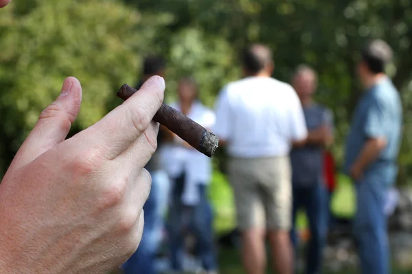 Рука с сигарой и многие люди на заднем плане вне фокуса — стоковое фото