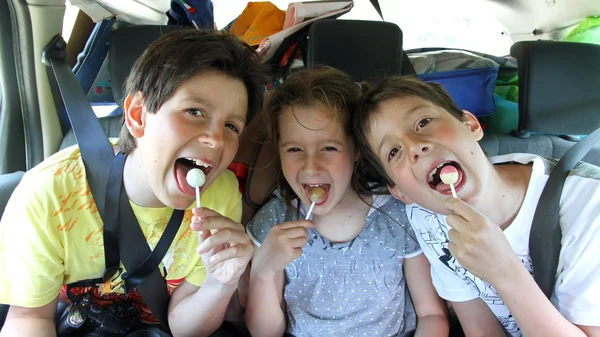 Tre fratelli felici mentre viaggiano in auto mangiando una caramella — Foto Stock