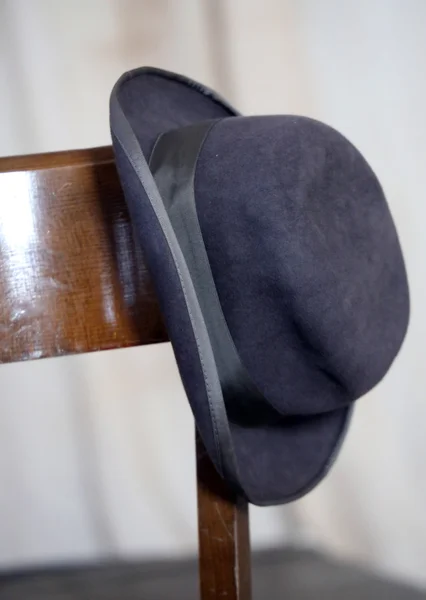 Old hat of an elder leaning on wooden chair — Stock Photo, Image