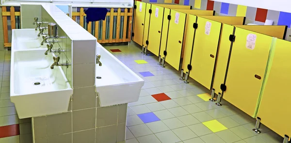 Bathroom of a nursery with white sinks and yellow toilet doors — Stock Photo, Image