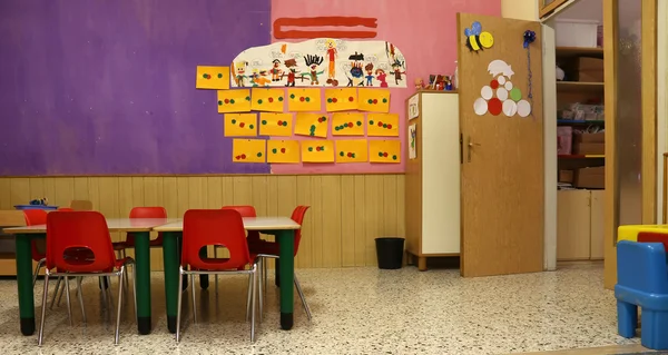 Sala de aula com cadeiras vermelhas e mesa com desenhos de crianças — Fotografia de Stock