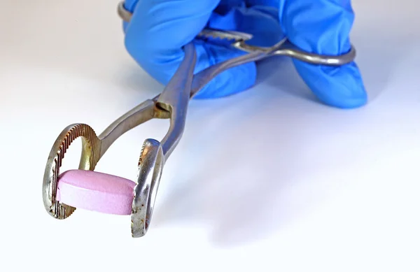 Comprimido rosa com fórceps médico e luva do médico — Fotografia de Stock