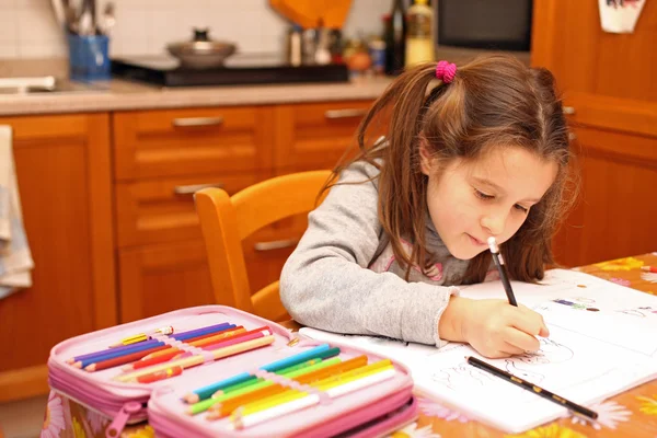 Niña escribe con lápiz en el libro de la escuela en la cocina — Foto de Stock