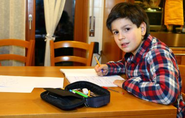 Young boy writes on his notebook at home clipart