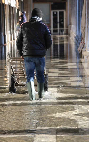 Transport cart and man with green boots at high tide — Stock Photo, Image