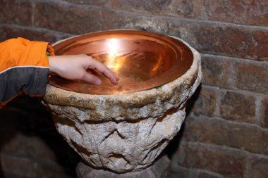 hand of child and an ancient holy water font  in a copper vase clipart
