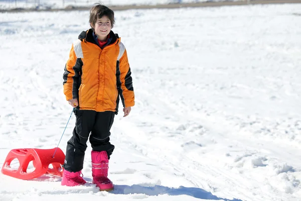 Child plays with sled  in the white snow — Stock Photo, Image