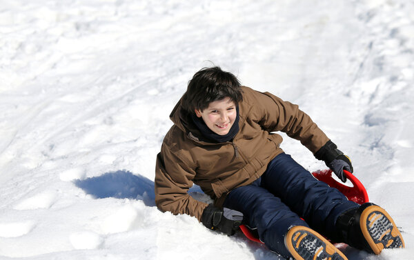 Парень играет с санками на снегу
