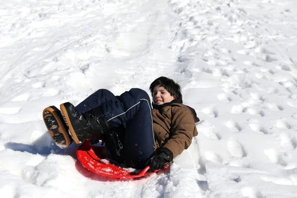 Pojke leker med kälkåkning på snö — Stockfoto