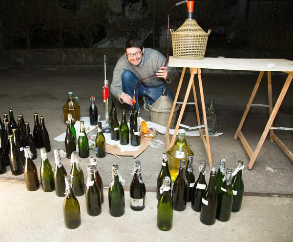 Homme embouteillant du vin rouge du demijohn aux bouteilles en verre — Photo