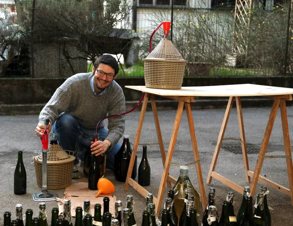 Man pour red wine from the demijohn to glass bottles — Stock Photo, Image