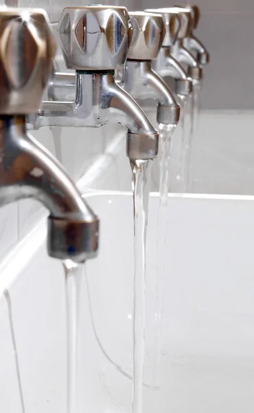 Rubinetti in acciaio con acqua potabile che scorre nel bagno del college — Foto Stock