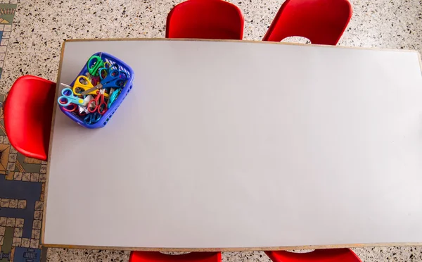 Rode stoelen en een tafel met een mandje van schaar in de kleuterschool — Stockfoto