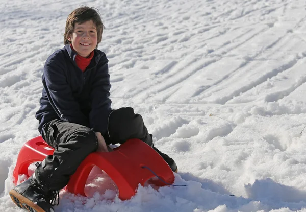 Jovem menino se divertindo no trenó vermelho nas montanhas em winte — Fotografia de Stock