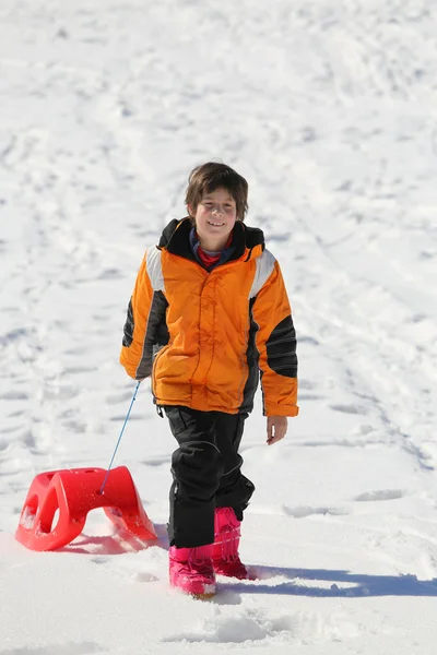 Boy having fun on the red sleigh in the mountains in winter — Stock Photo, Image