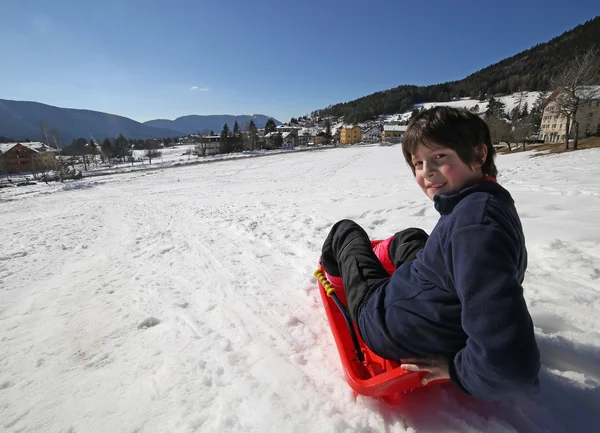 Young boy having fun on the red sleigh in the mountains — Stock Photo, Image