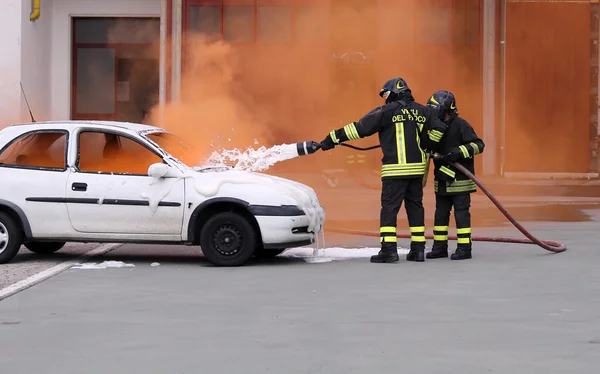 Firefighters during exercise to extinguish a fire in a car Stock Picture