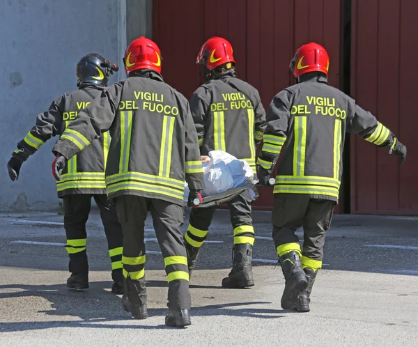 Cuatro bomberos en acción llevan una camilla con heridos — Foto de Stock