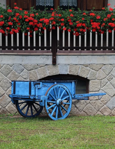 Blauer Holzwagen mit Geranien auf dem Hof — Stockfoto