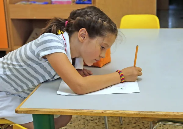 Child writes on paper with pencil in classroom — Stock Photo, Image