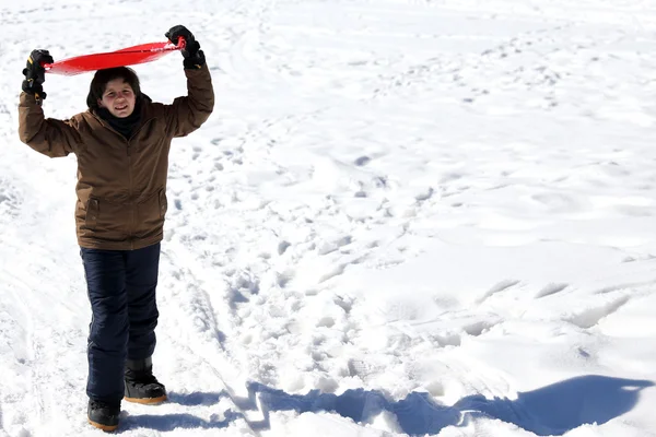 Ragazzo con la slitta di neve rossa in inverno — Foto Stock