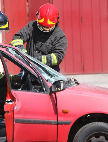Chief fireman whit red helmet while breaking the windshield — Stockfoto