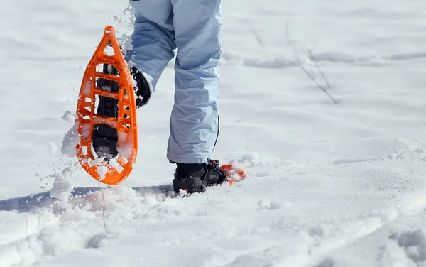 woman walking with two orange snowshoes in mountains in winter