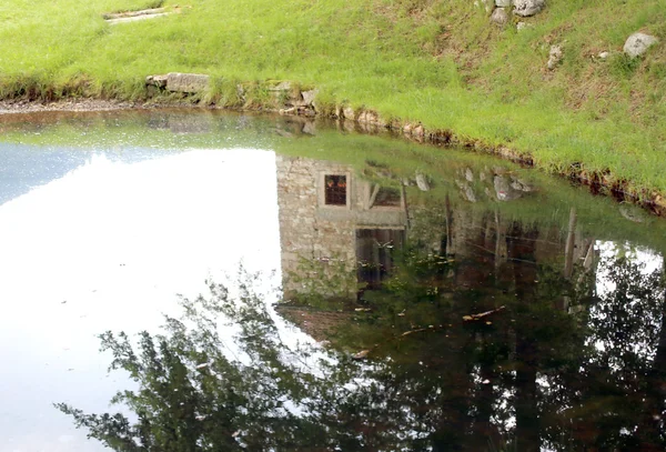 Reflejo de una antigua casa de montaña en el estanque — Foto de Stock