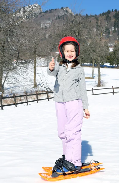 Young girl with orange snowshoes and helmet — 图库照片