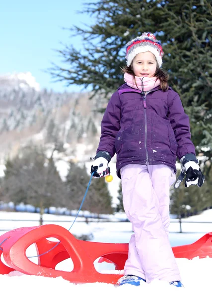 Pretty girl plays with red sled in the mountains in the snow — 图库照片